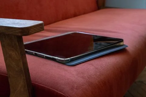 Tablet computer resting on a red upholstered chair in protective cover. Por.. Stock Photos