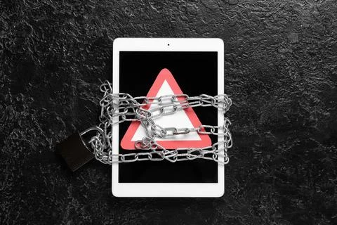 Tablet computer with warning sign and chains on dark background. Crime concep Stock Photos
