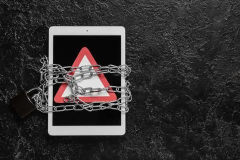 Tablet computer with warning sign and chains on dark background. Crime concep Stock Photos