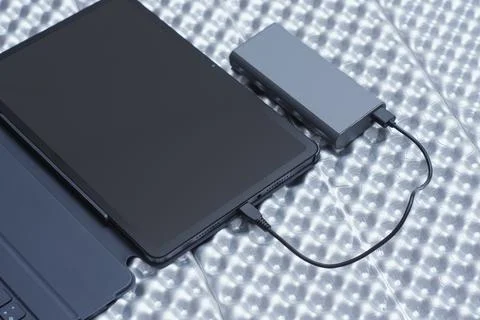 Tablet connected to a power bank using a USB cable on a textured background.. Stock Photos