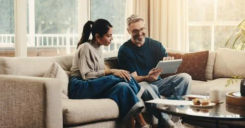 Tablet, conversation and couple on sofa in home with planning budget, savings or Stock Photos