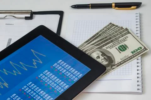 Tablet with an economic image on a pile of dollars and sheets of statistics Stock Photos
