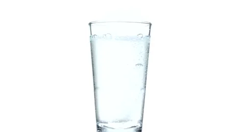 Tablet falling and dissolving into a glass of water against white background Stock Footage 234885942