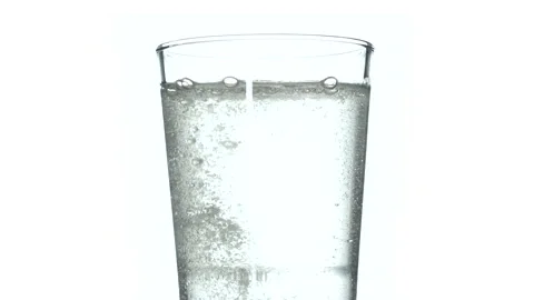 Tablet falling and dissolving into a glass of water against white background Stock Footage 234886459