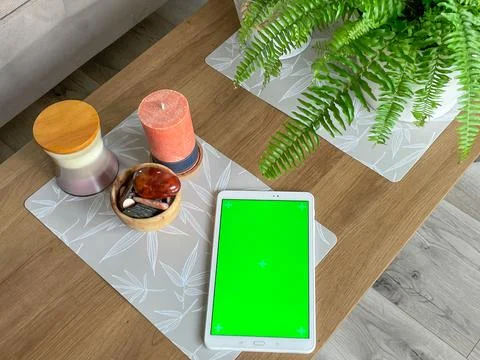 Tablet with green screen laying on table near candle, natural stones and plan Stock Photos