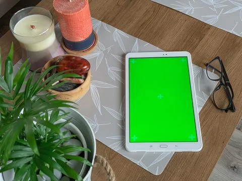 Tablet with green screen laying on table near candle, natural stones and plan Stock Photos