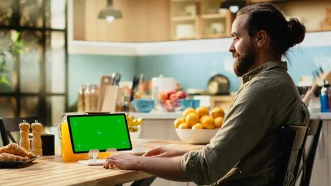 Tablet, green screen mockup, kitchen wooden table, male working from home Stock Photos