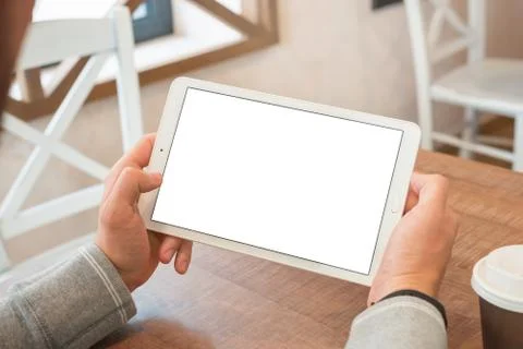 Tablet in hands closeup. Blank screen for mockup. Table, coffee, chairs in ba Stock Photos