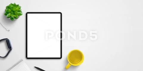Tablet mockup on desk surrounded by watch, coffee mug, pad, plant and pen. Copy PSD Template