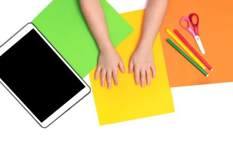 Tablet, multi-colored sheets of paper and the hands of a child on the table. Foto stock