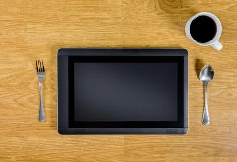 Tablet over wood table with spoon, fork and coffee cup Stock Photos