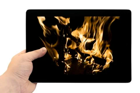 Tablet PC in hand with flames of burning fire background on screen isolated o Stock Photos