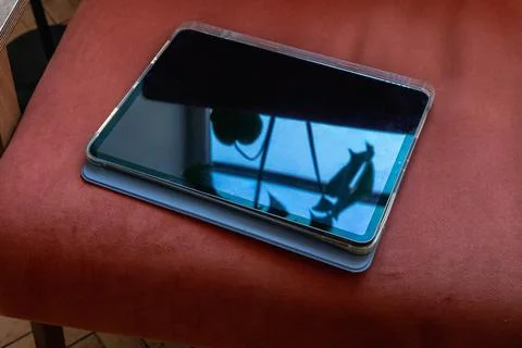 Tablet with reflective blank screen resting on upholstered chair. Portable .. Stock Photos