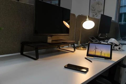 Tablet on stand is displaying wind turbines at sunset on white desk, brass lamp Stock Photos