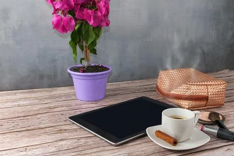 Tablet on the table surrounded by coffee cup, lipstick and makeup bag side vi Stock Photos