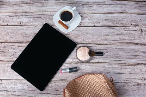 Tablet on the table surrounded by coffee cup, lipstick and makeup bag top vie Stock Photos