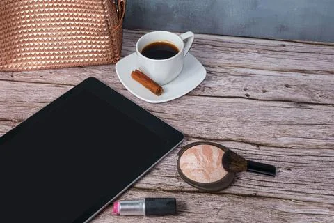 Tablet on the table surrounded by lipstick, pressed powder, coffee cup and ma Stock Photos