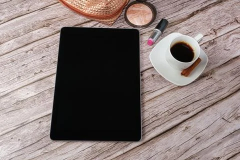 Tablet on the table surrounded by makeup bag, lipstick and coffee cup. Stock Photos