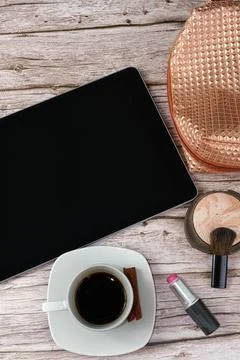 Tablet on the table surrounded by makeup bag, lipstick and coffee cup top vie Stock Photos