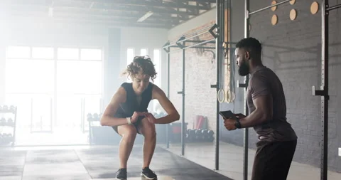 Tablet tapping trainer cueing woman athlete squatting and jumping onto box at Stock Footage 314043799