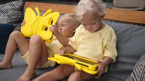 Tablet time for twin toddlers, each with its own yellow cased tablet relaxing Stock Footage 159941948