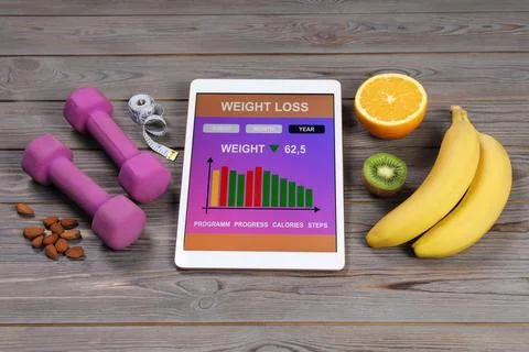 Tablet with weight loss calculator application, dumbbells and products on g.. Foto stock