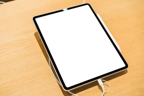 Tablet on a wooden table with charging cable and white screen Stock Photos