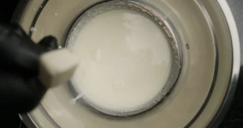 TABLETOP slowmotion shot: chef adds sliced butter to the hot milk in metal bowl Stock Footage 131306645
