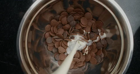 TABLETOP slowmotion shot: chef chocolatier adds hot milk to the metal bowl with Stock Footage 131339509