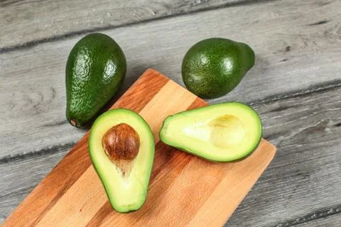 Tabletop view, chopping board on gray wood desk, avocado cut in half, with se Stock Photos