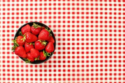 Tabletop view, small black ceramic bowl of strawberries on red chequered ging Stock Photos