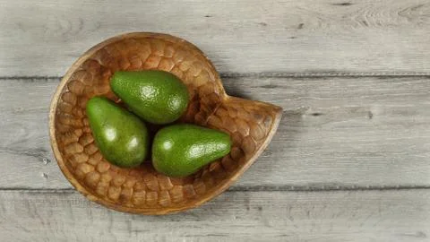 Tabletop view, three avocado pears on wooden carved bowl Stock Photos