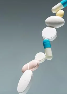 Tablets and capsules stack in midair on gray gradient background, clean minim Stock Photos