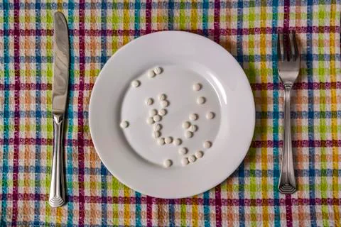 Tablets are on a plate next to a fork and spoon.concept of disease and treatm Stock Photos