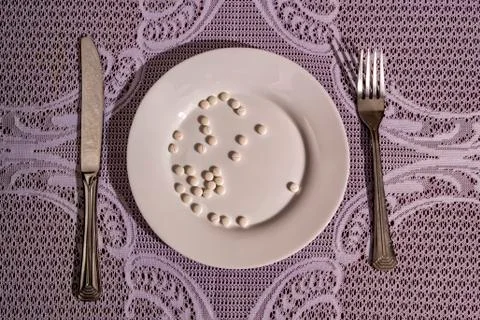 Tablets are on a plate next to a fork and spoon.concept of disease and treatm Stock Photos