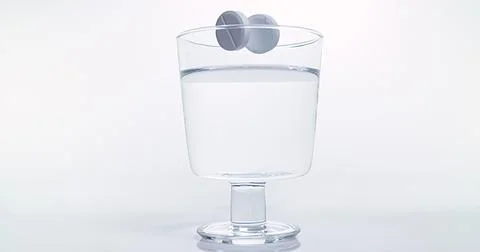 Tablets Falling and Dissolving into a Glass of Water against White Background Stock Photos