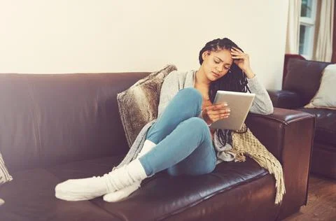 Tablets make binge-watching so much easier. a young woman using her tablet while Stock Photos