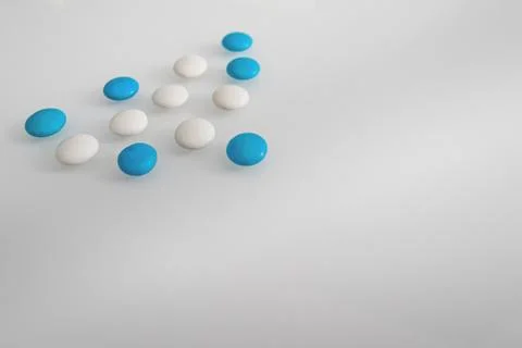 Tablets or sweets, white and colored on a white glass table Stock Photos