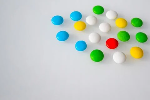Tablets or sweets, white and colored on a white glass table Stock Photos