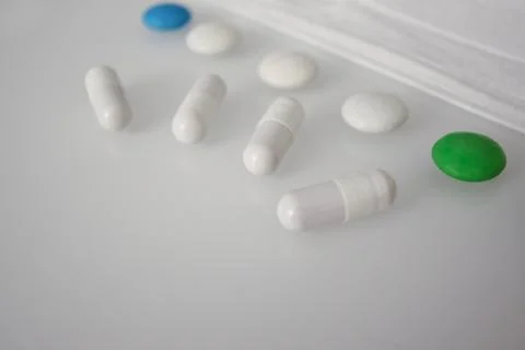 Tablets or sweets, white and colored on a white glass table Stock Photos