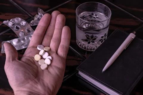 Tablets in a person's hand against a background of empty blisters, a glass of Stock Photos