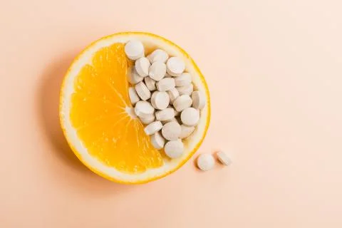 Tablets with vitamins in an orange slice on a beige background. Stock Photos