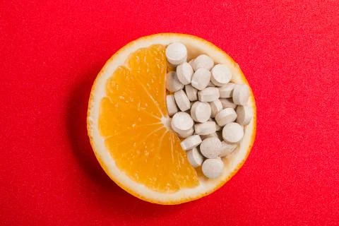 Tablets with vitamins in an orange slice on a red background. Stock Photos