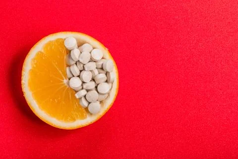Tablets with vitamins in an orange slice on a red background. 写真素材