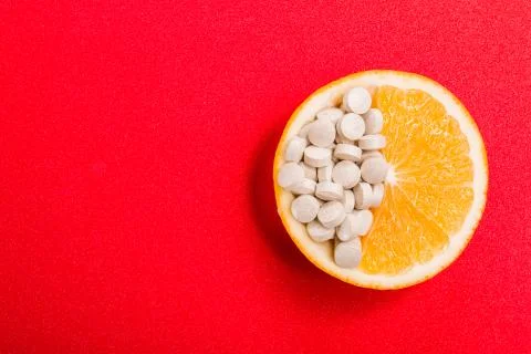 Tablets with vitamins in an orange slice on a red background. Stock Photos
