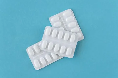 Tabletts or pills in white package on the blue paper background. Stock Photos