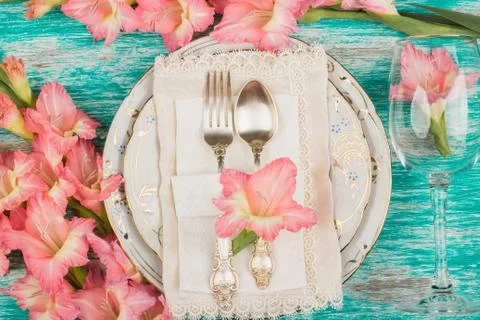 Tableware and silverware with light pink gladiolus on the azure background Stock Photos