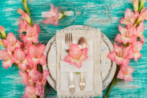 Tableware and silverware with light pink gladiolus on the azure background Stock Photos
