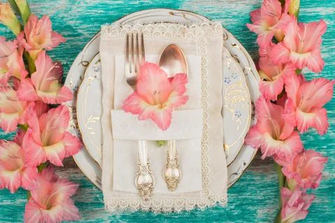 Tableware and silverware with light pink gladiolus on the azure background 库存照片