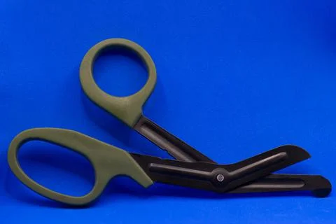 Tactical scissors opened on a blue background with dark green handles. Stock Photos